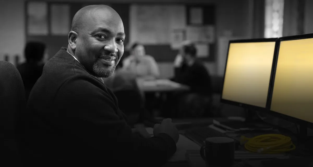 A smiling professional at his desk in an open-plan office