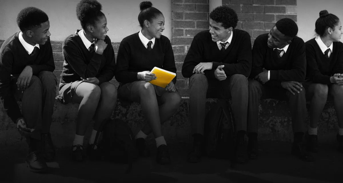 Six learners in school uniform sitting on a wall, talking and laughing
