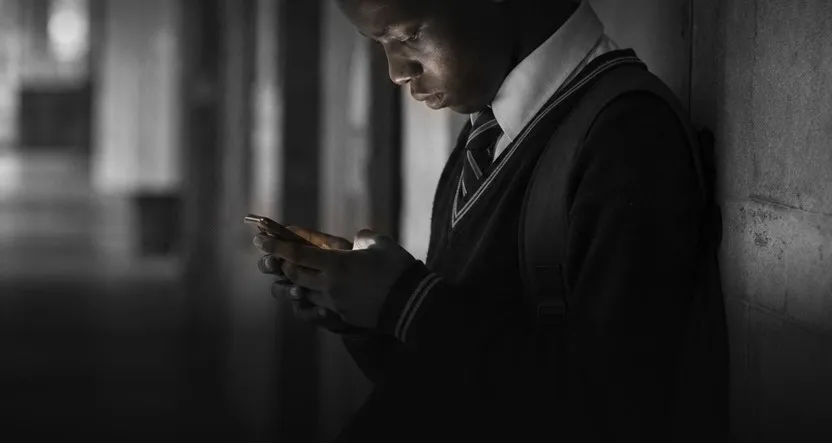 A learner in school uniform reading his phone in a corridor