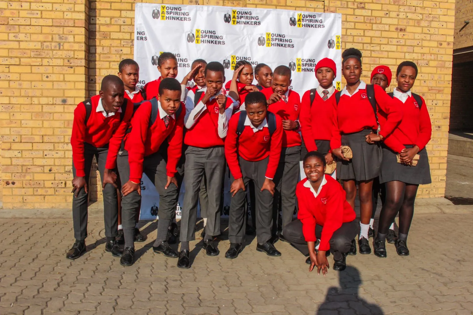 Learners in red school uniform in front of a YAT banner at their school